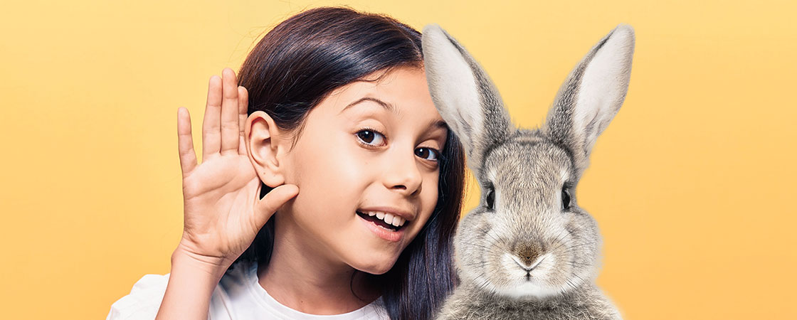 a girl holding her hands up next to her ear and sitting next to a rabbit